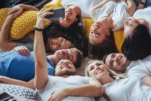 grupo de jóvenes hermosos haciendo selfie tirados en el suelo, mejores amigos niñas y niños juntos divirtiéndose, planteando un concepto de estilo de vida emocional foto