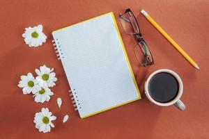 On wooden background notebook pencil, coffee and flowers. photo