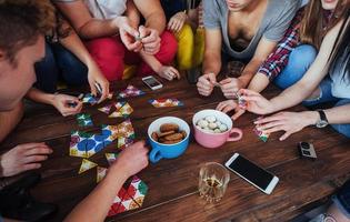 Top view creative photo of friends sitting at wooden table.  having fun while playing board game