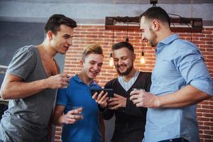 Cheerful old friends communicate with each other and phone watch,  glasses of whiskey in pub. Concept  entertainment  lifestyle. Wifi connected people in bar table meeting photo