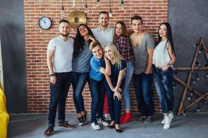 Group portrait of multi-ethnic boys and girls with colorful fashionable clothes holding friend posing on a brick wall, Urban style people having fun, Concepts about youth togetherness lifestyle photo