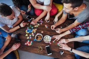 Top view creative photo of friends sitting at wooden table.  having fun while playing board game