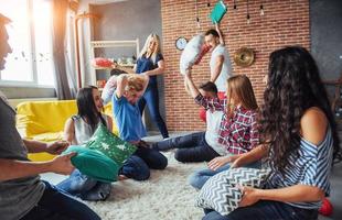 Crazy young best friends fighting pillows at home. Mixed race group of people. Concept  entertainment and lifestyle photo