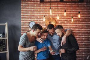 viejos amigos alegres se comunican entre sí y miran por teléfono, vasos de whisky en el pub. concepto de estilo de vida de entretenimiento. personas conectadas wifi en una reunión de mesa de bar foto