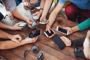 Top view hands circle using phone in cafe - Multiracial friends mobile addicted interior scene from above - Wifi connected people in bar table meeting - Concept of teamwork photo