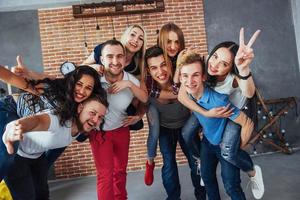 Group portrait of multi-ethnic boys and girls with colorful fashionable clothes holding friend posing on a brick wall, Urban style people having fun, Concepts about youth togetherness lifestyle photo