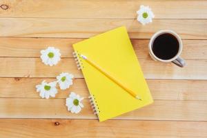 sobre fondo de madera cuaderno lápiz, café y flores. foto