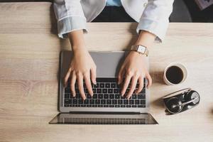 Top view of woman hand are typing on laptop keyboard with coffee and alarm clock on a wooden office desk photo