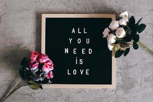 Quote on letter board says All you need is love with colorful rose flower photo