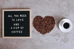 Top view of a cup of coffee and heart shape from coffee beans with quote on letter board, all you need is love and a cup of coffee photo