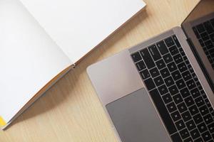 Top view of blank book open with laptop on wooden table photo