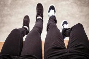 Couple leg wearing black pants sitting with legs hanging to the ground photo