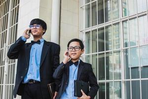 Two teenager with vintage black suit  are talking on the phone while smiling and holding notebook photo