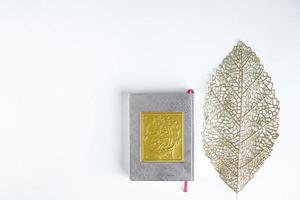 Flat lay gold Arabic on book of holy Quran and gold leaves on white background with copy space, Bandung Indonesia, March 2021 photo