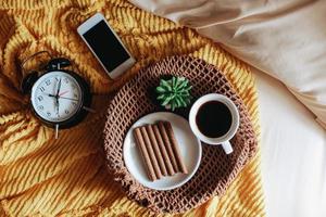 Tasty snack and a cup of coffee for breakfast with clock showing 7 o'clock on the bed photo