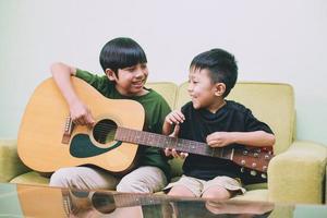 dos niños asiáticos tocando la guitarra y divirtiéndose juntos en casa foto