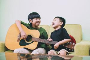 dos hermanos asiáticos divirtiéndose juntos cantando y tocando la guitarra foto