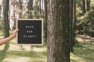 mano sosteniendo un tablero de cartas que dice salvar nuestro planeta en el bosque, concepto del día de la tierra. foto