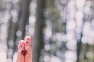 Red heart shape on two fingers with face image while smiling face with nature bokeh background. copy space. Happy couple in love. photo