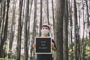 A boy showing quote on letter board says save our planet with forest on the background, earth day concept photo