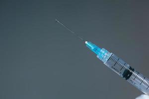 Close up of medical syringe with vaccine droplet on the needle. Selective focus photo