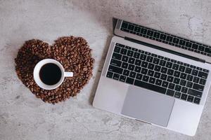 Top view of a cup of coffee on beautiful heart shape from coffee beans with laptop photo