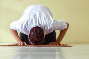 vista frontal del hombre musulmán haciendo salat con pose de postración en la alfombra de oración foto