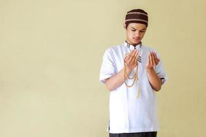 Young asian muslim man praying while holding rosary beads with copy space