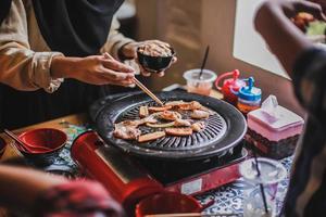 Hand of people cooking barbecue meat with chopsticks. Concept of summer party with families and friends photo