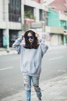 Fashionable woman wearing sweater with hood and sunglasses walking on the city street photo