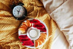 Various fruit for breakfast with clock showing 7 o'clock on the bed photo