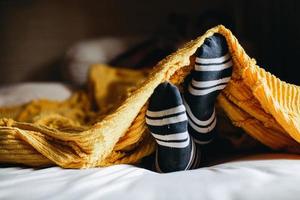 Cozy position of foot in warm socks under the blankets on the bed photo