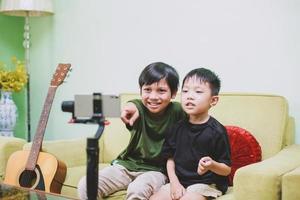dos niños asiáticos youtuber sonriendo e interactuando con su audiencia en el teléfono mientras hacen transmisión en vivo foto