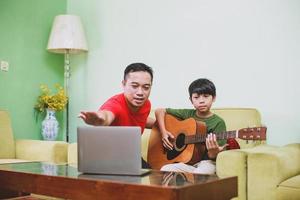 Asian father shows how to play guitar to his son with laptop photo