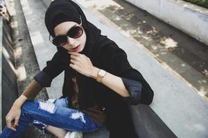 Stylish muslim woman with black headscarf wearing sunglasses and black coat photo