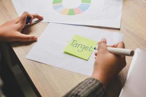 Woman hand writing word Target in a yellow sticky note with black felt-tip pen on office desk. Business concept photo
