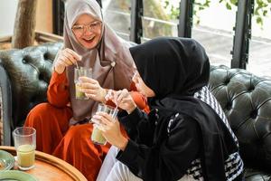 Two muslim sisters joking and holding avocado juice at the cafe photo