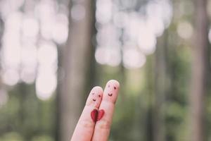 Red heart shape on two fingers with face image while smiling face with nature bokeh background. copy space. Happy couple in love. photo