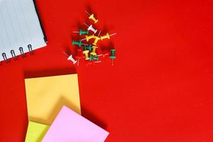 Top view of office or school supplies isolated on red background. Open book, colorful push pin and sticky note with free or copy space photo