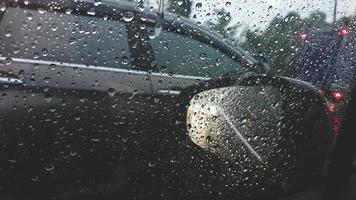 Rain falling on car windows view with Reflection of traffic flow from car rear view mirror with water drop at heavy rain photo