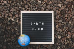 Quote on letter board says Earth hour and earth globe with rock background photo