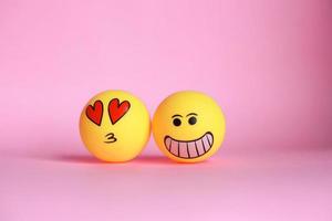 Smiley emoticon and love on face emoticon with mouth kissing isolated on pink background. photo