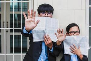 Two teenager doing stop gesture and covered their mouths by newspapers. Stop Hoax or fake news Concept photo