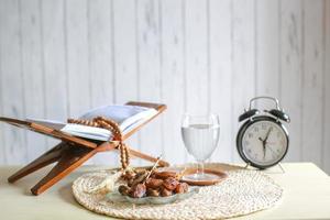 kurma o fruta de dátiles con un vaso de agua mineral, libro sagrado al-quran, despertador y cuentas de oración sobre la mesa. Ramadán tradicional, comida iftar. concepto de mes de ayuno ramadan kareem foto