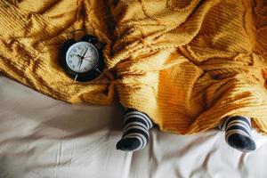 People sleeping on a bed under the blankets and warm socks with alarm clock showing 7 o'clock on the side photo