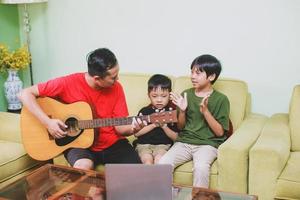 padre e hijo asiáticos tocando la guitarra y cantando junto con su hijo en casa foto