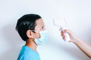 termómetro infrarrojo de mano que mide la temperatura del niño con máscara médica en la cara foto