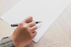 primer plano de las manos de la mujer escribiendo en papel colocado en un escritorio de madera con espacio para copiar. concepto de educación y negocios. hacer planes y listas foto