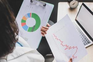 Business woman reading and checking business graph. Female worker analyzing graph and chart on clip board in modern office photo