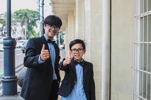 Two teenager wearing vintage black suit posing and smiling into the camera while showing thumb up or like gesture photo